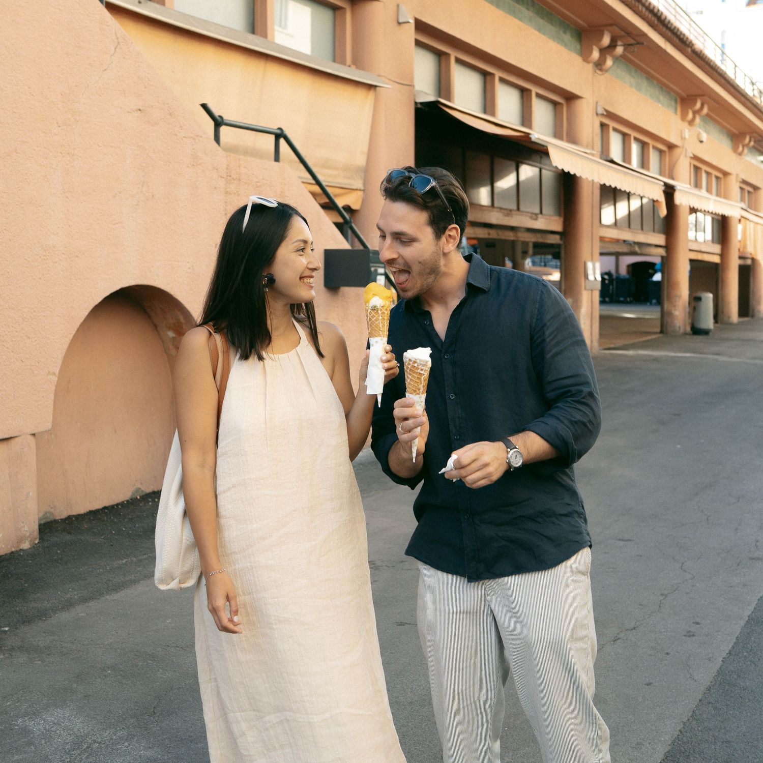 Couple in casual attire walking and laughing together on a terrace with peach-colored walls in the background.
