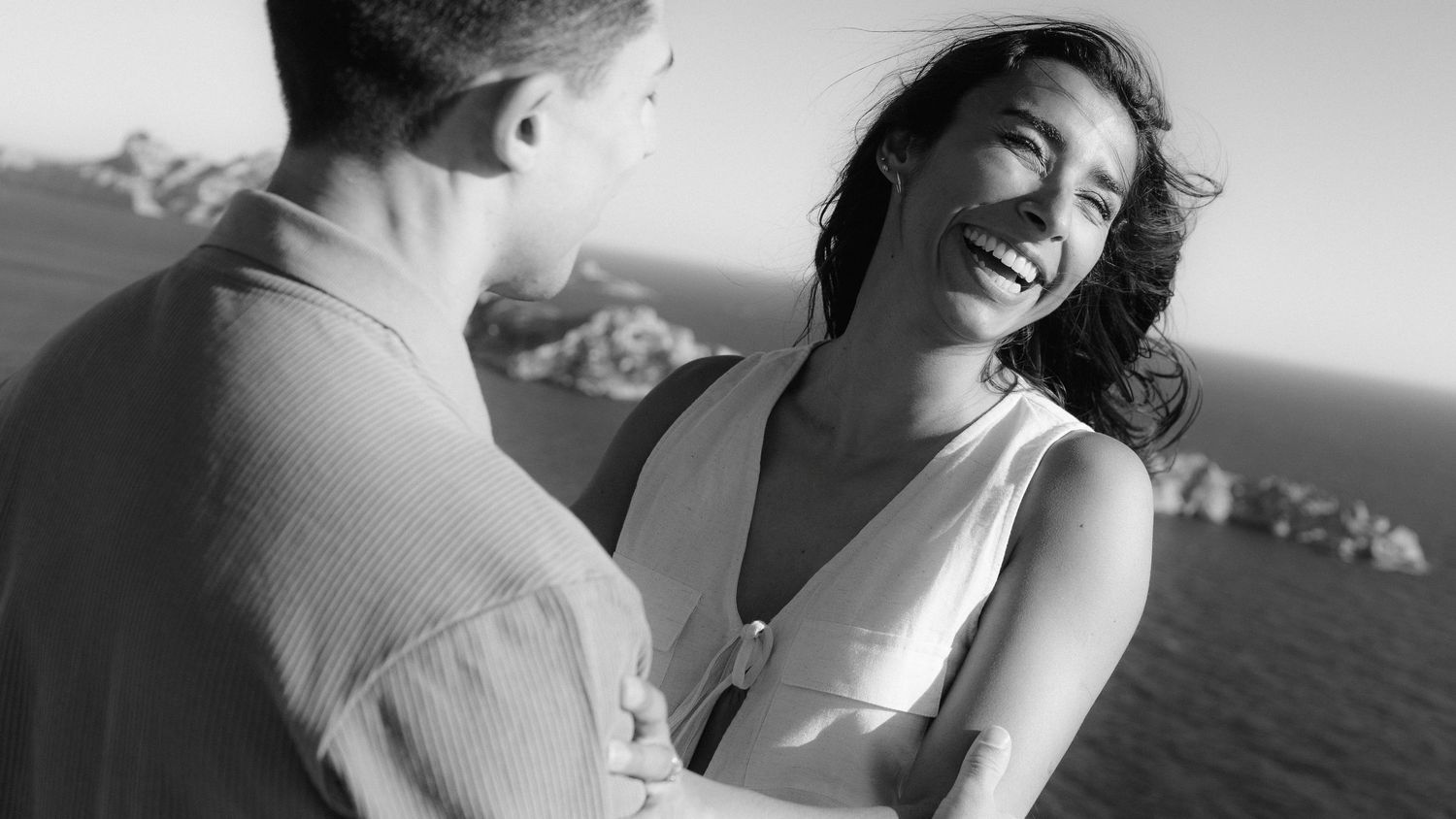 A couple embraces intimately in black and white photography on a scenic coastal overlook.