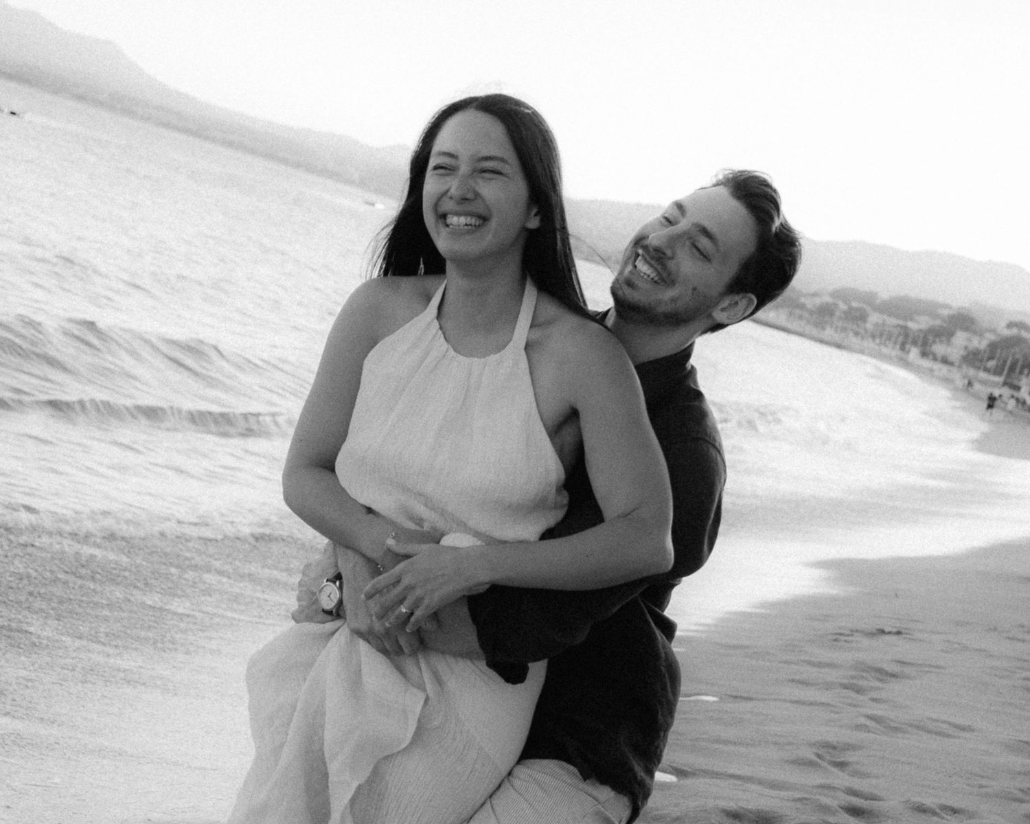 A couple embraces joyfully on the beach in black and white photos showing moments of happiness and laughter.