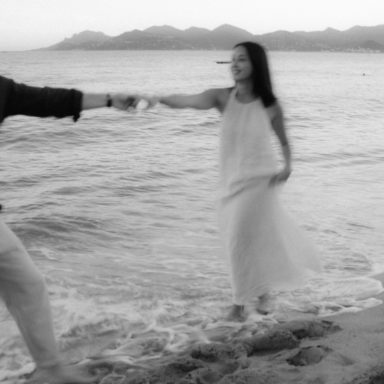 A person in a white dress twirls gracefully on a beach with ocean waves in the background, creating a dreamy scene.