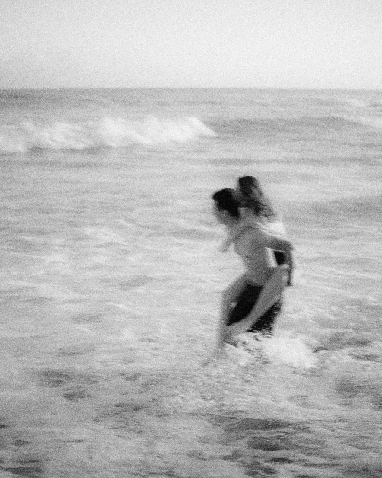 A sequence of black and white photos showing a figure running and splashing through ocean waves at the beach.