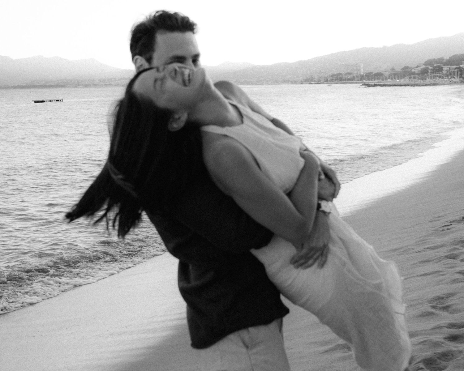 A couple embraces romantically on a beach at sunset creating silhouettes against the ocean backdrop.