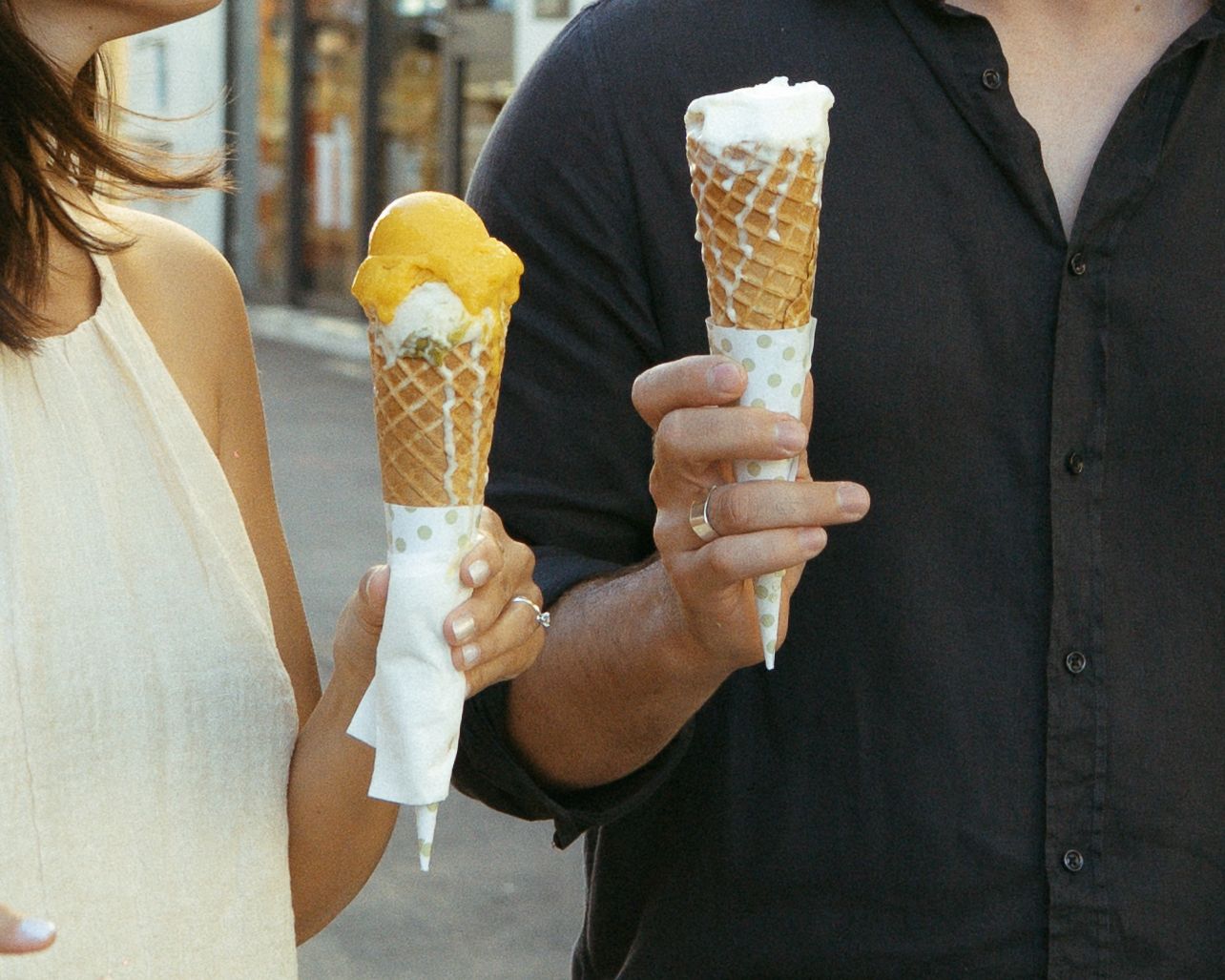 Group of people enjoying ice cream cones on a sunny day while wearing casual attire.