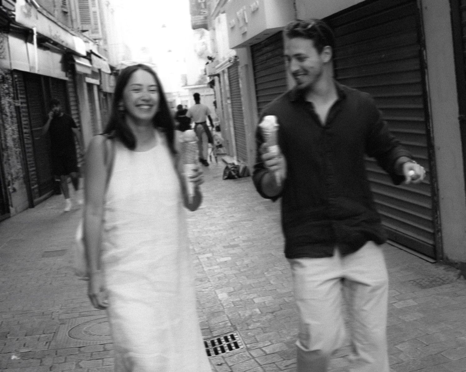 A sequence of black and white photos showing a couple walking and laughing together on a narrow European street.