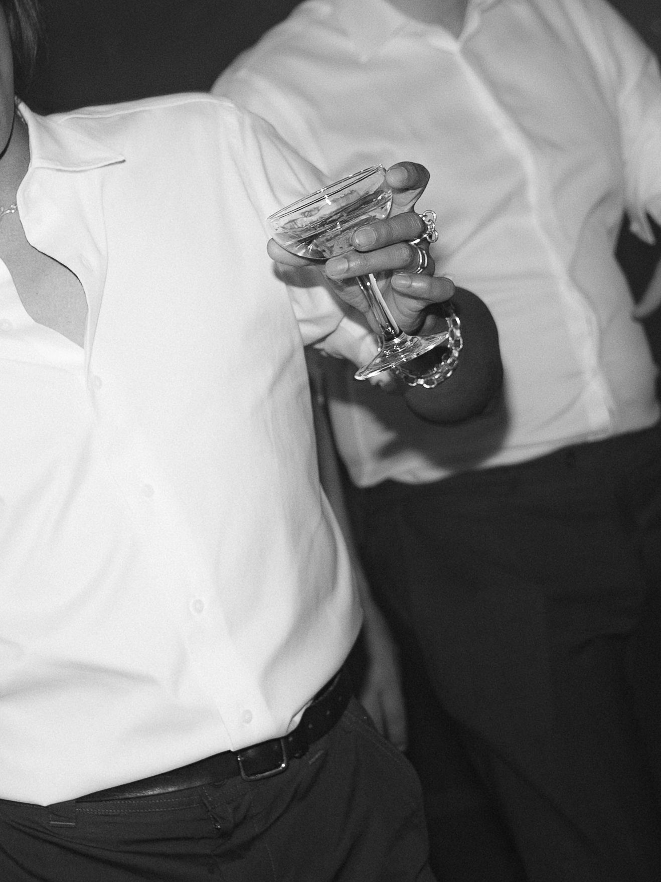 Black and white photo of two people in white shirts, one holding a martini glass at a social event.