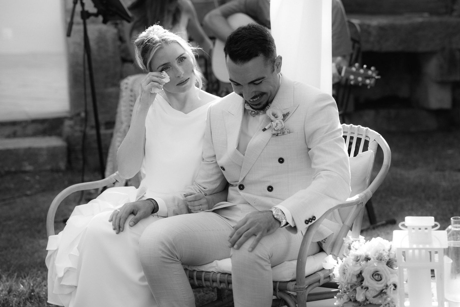 Black and white photo of a bride wiping tears and groom bowing head during an emotional outdoor wedding ceremony.