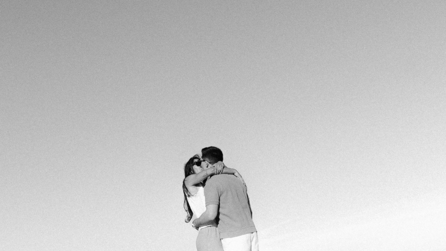 A couple embraces in a romantic silhouette against a minimalist gray sky background.