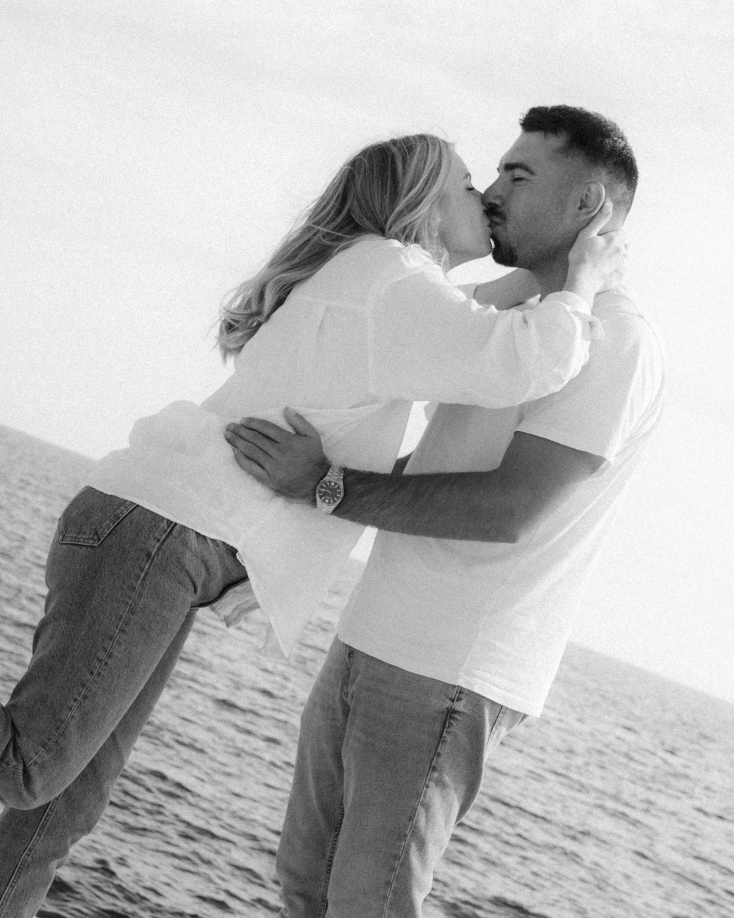 A couple embraces romantically on a beach in black and white, creating a series of intimate silhouetted moments.