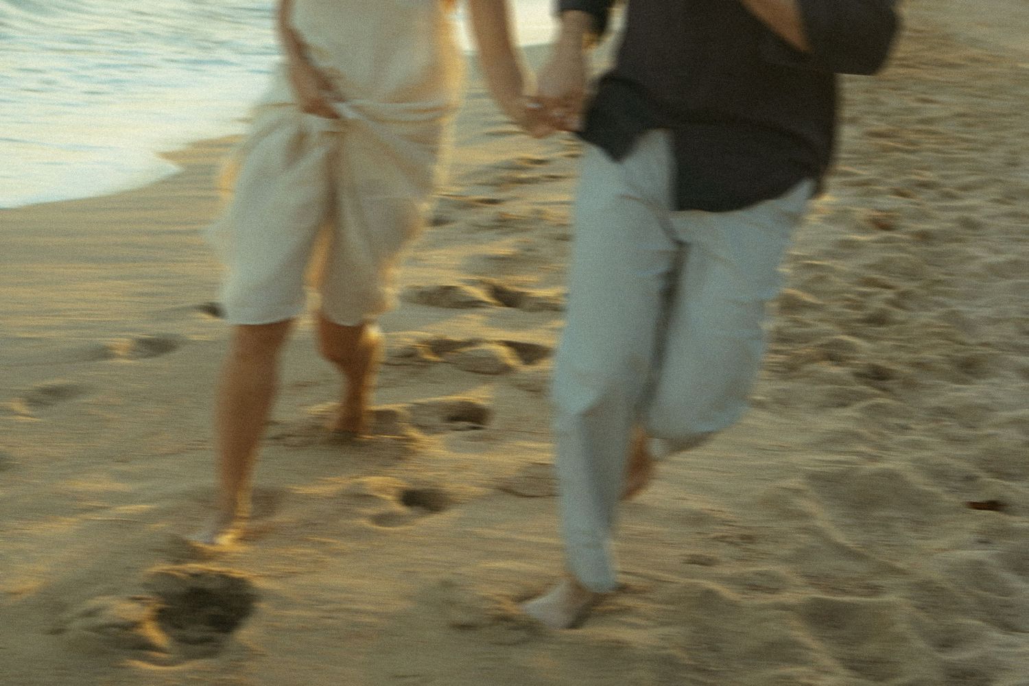 Two people walking together on a sandy beach during sunset with footprints trailing behind them.