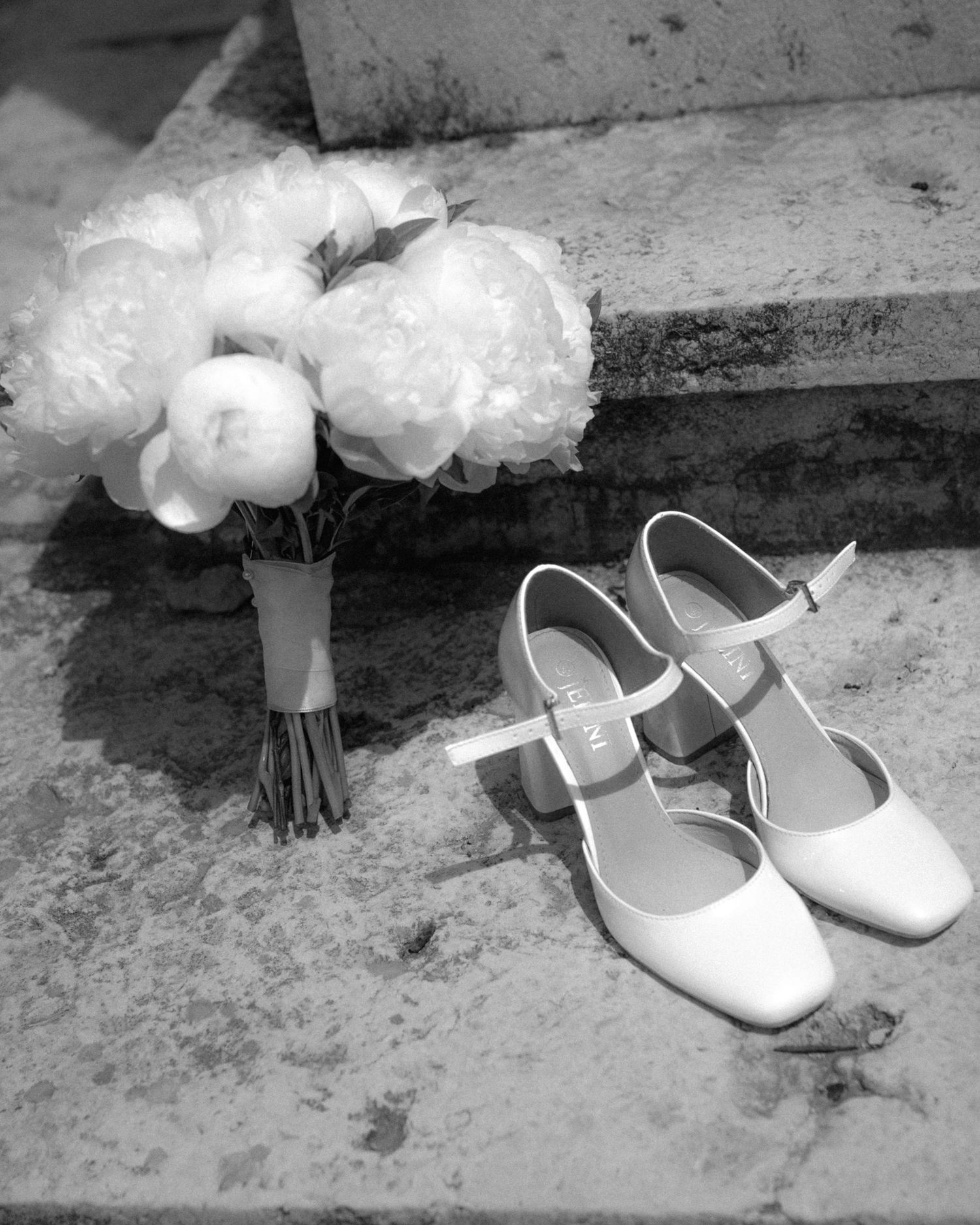 A sequence of black and white photos showing white wedding shoes and a bridal veil arranged on a textured surface.