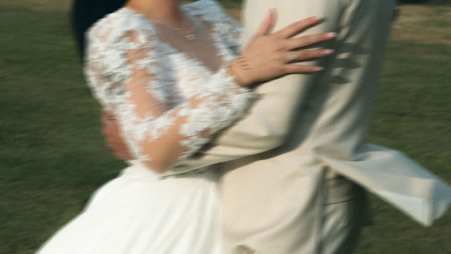 A couple in formal wedding attire shares a romantic kiss in a sunlit garden setting.