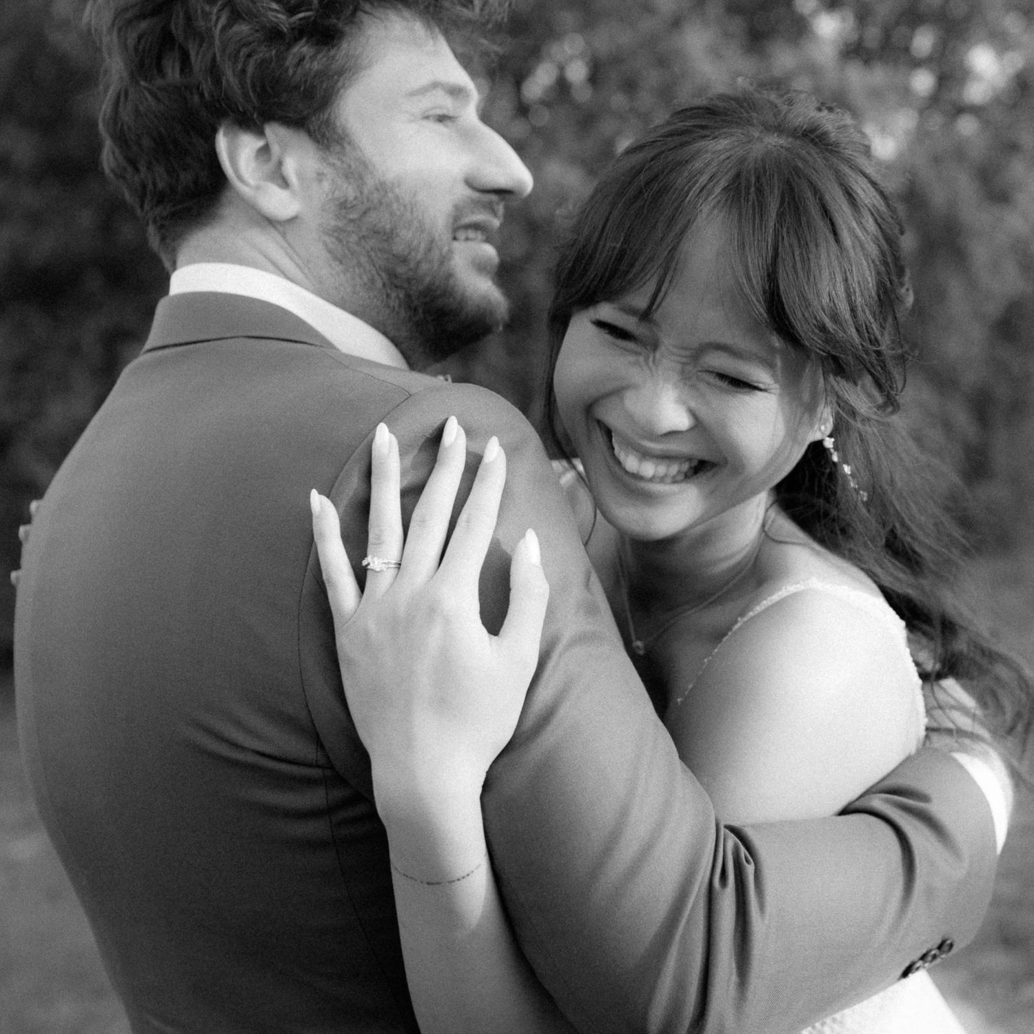 Black and white portrait of a happy couple embracing and laughing together during a romantic moment outdoors.