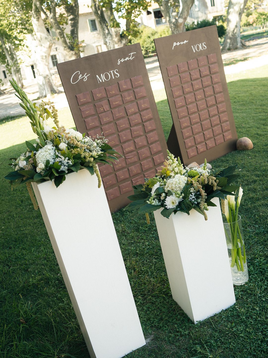 Elegant wedding seating chart displays on white pedestals with floral arrangements in a garden setting.