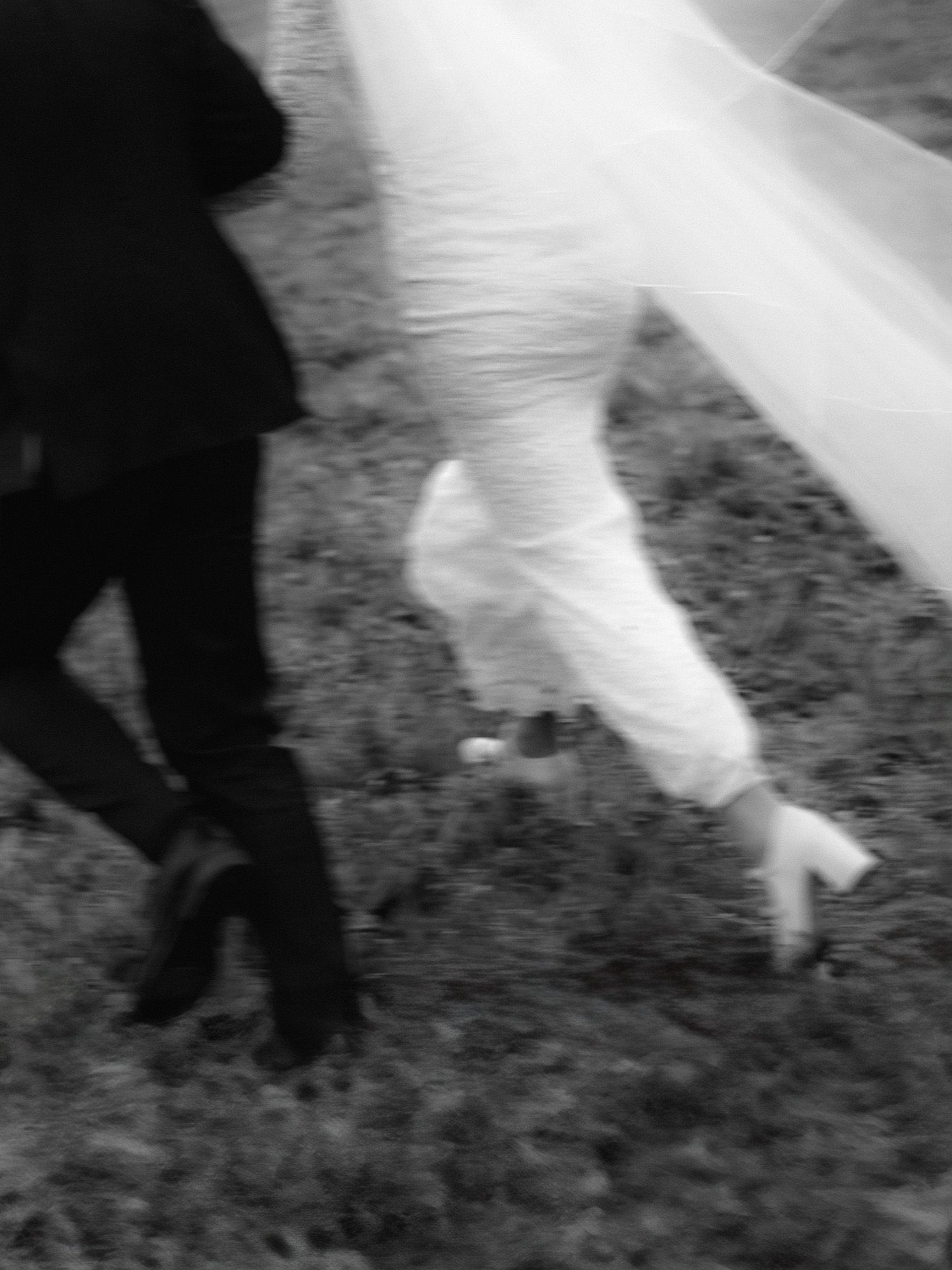Black and white photo of a bride in white dress and groom in dark suit walking on grass, motion blur effect.