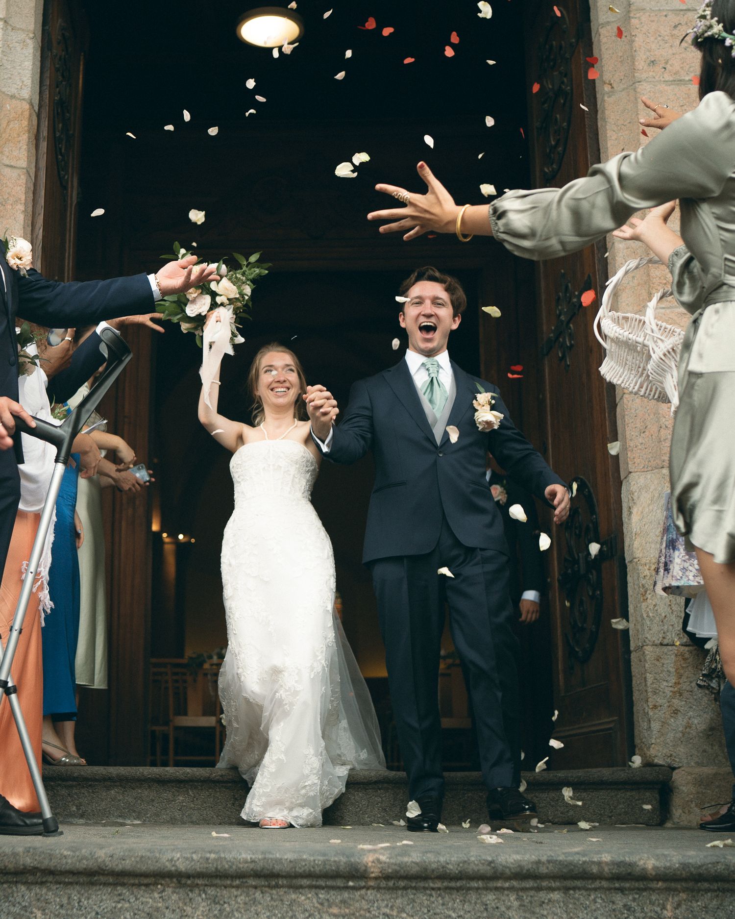 Newlyweds exit church as wedding guests shower them with flower petals and confetti in joyous celebration.