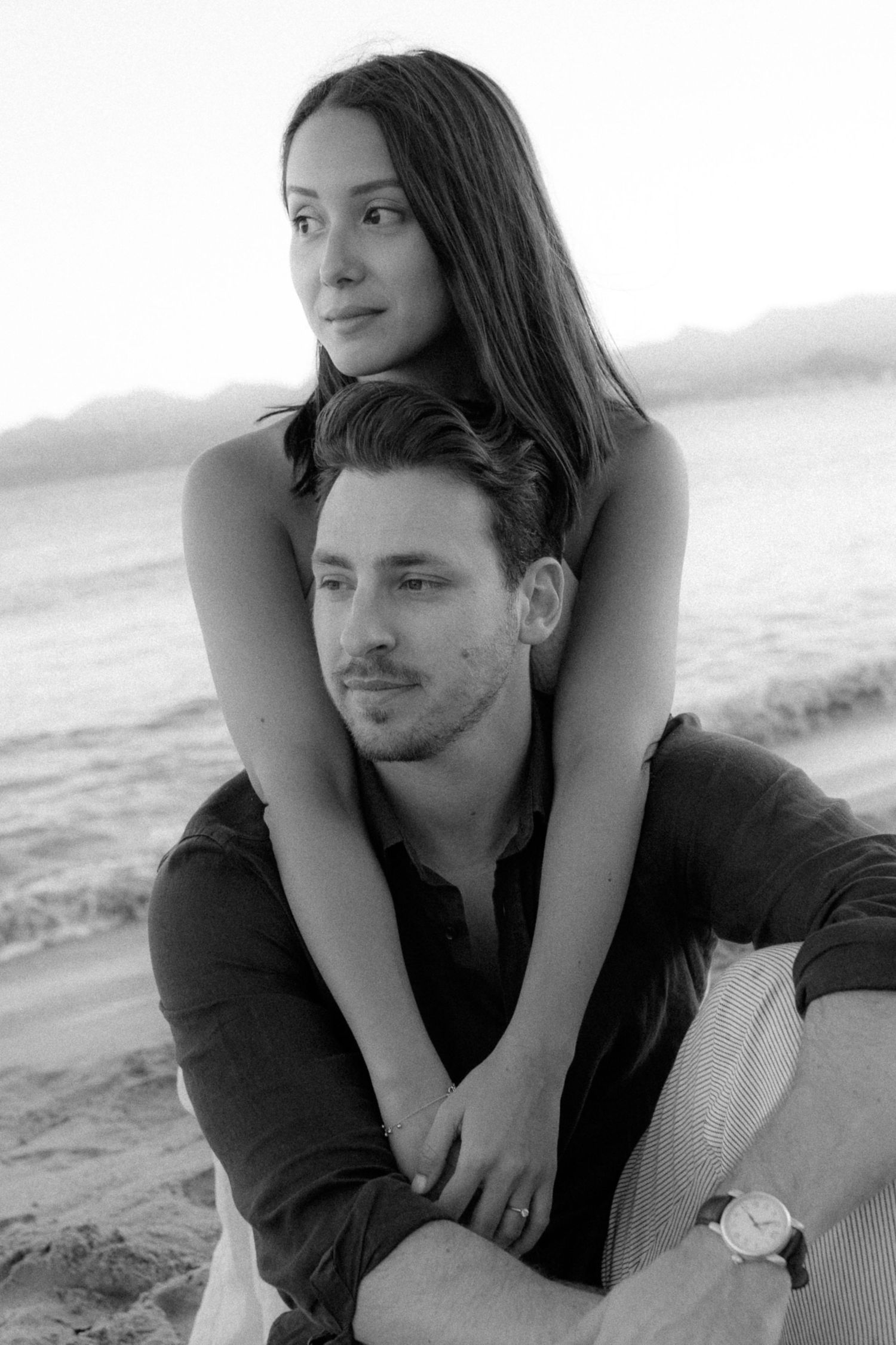Black and white romantic beach photoshoot of a couple embracing and posing together by the ocean.