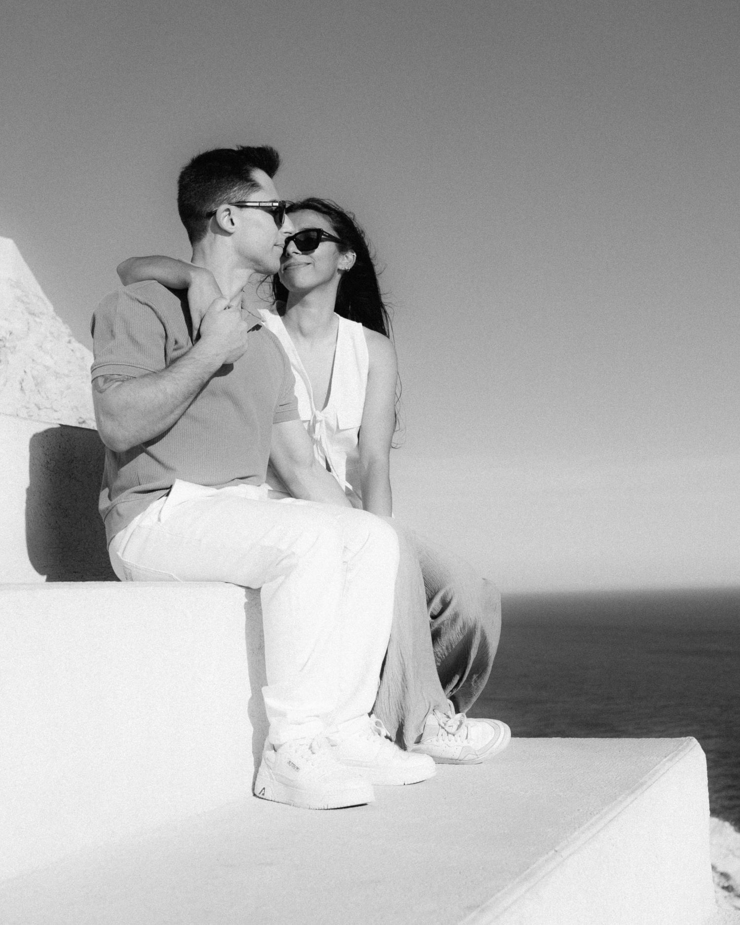 A romantic couple embraces intimately on a white surface in a black and white artistic photoshoot series.