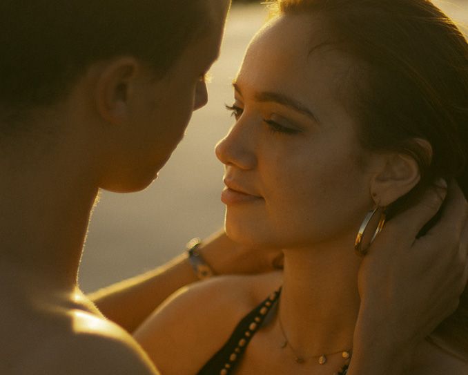 Romantic couple in warm sunset lighting share an intimate moment with golden glow illuminating their faces.