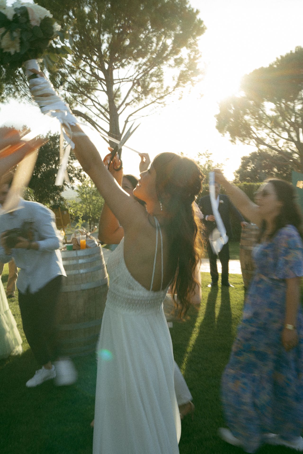 People celebrating at an outdoor wedding reception during golden hour with trees in the background.