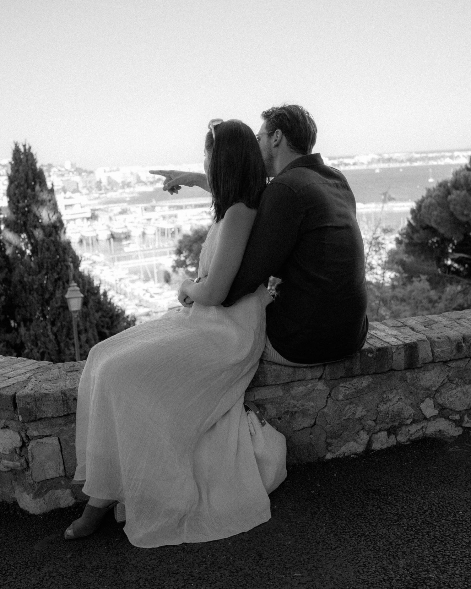 A romantic couple sits together on a stone wall overlooking a scenic vista in a series of black and white photos.