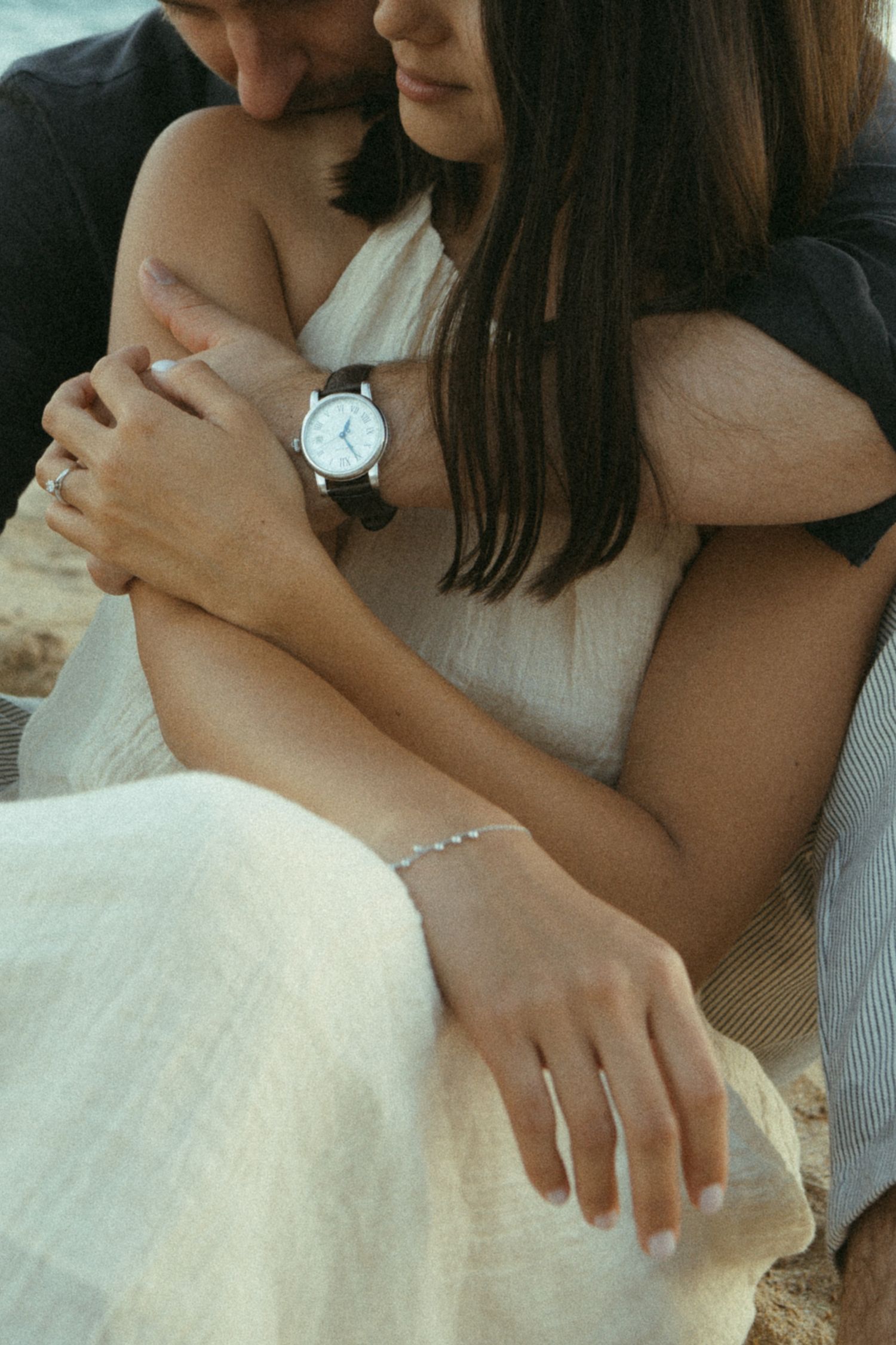 Close-up view of hands wearing a delicate silver bracelet and white dress against a neutral background.