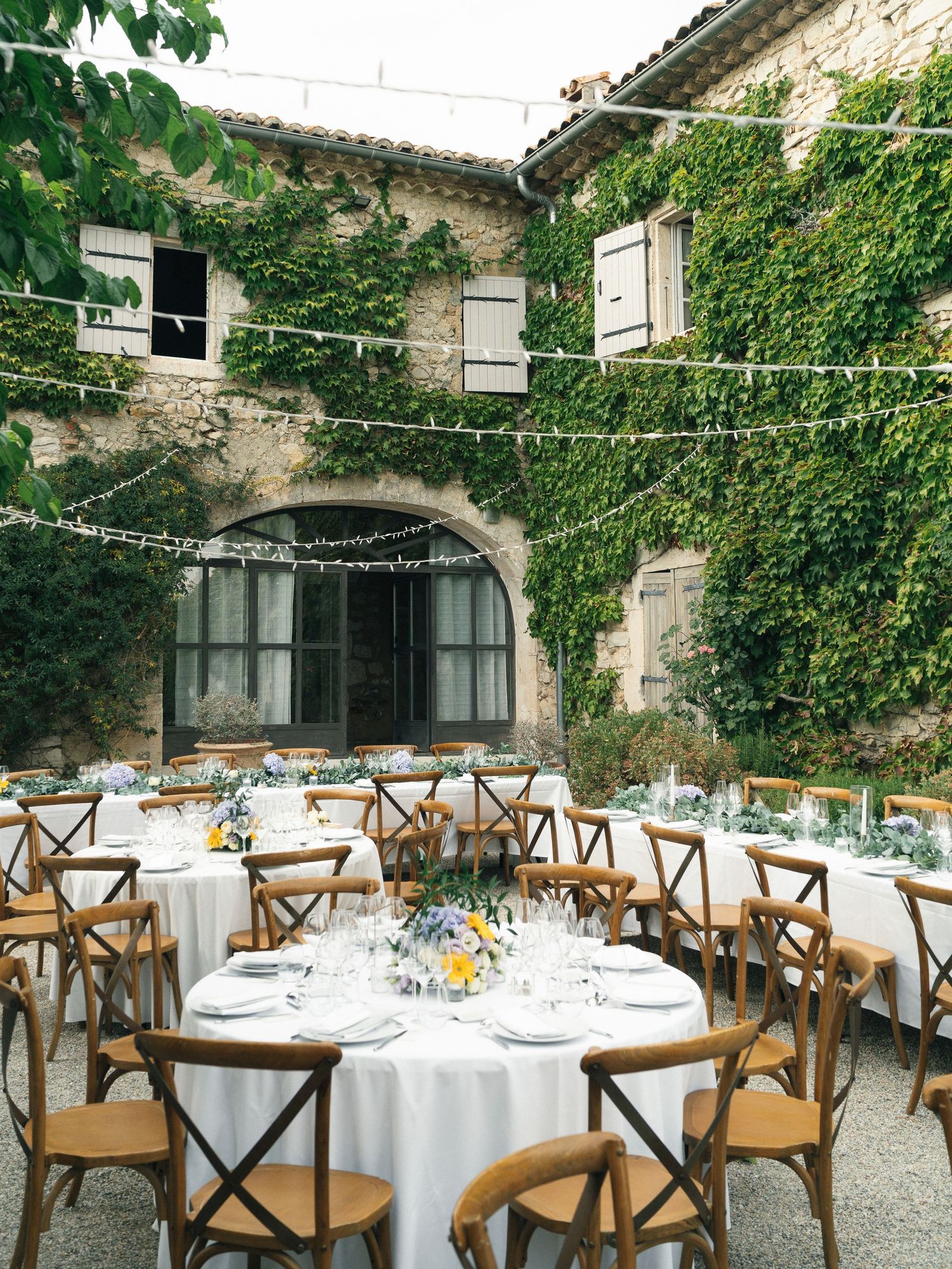 Elegant outdoor wedding reception in ivy-covered stone courtyard with round tables, white linens, and string lights.