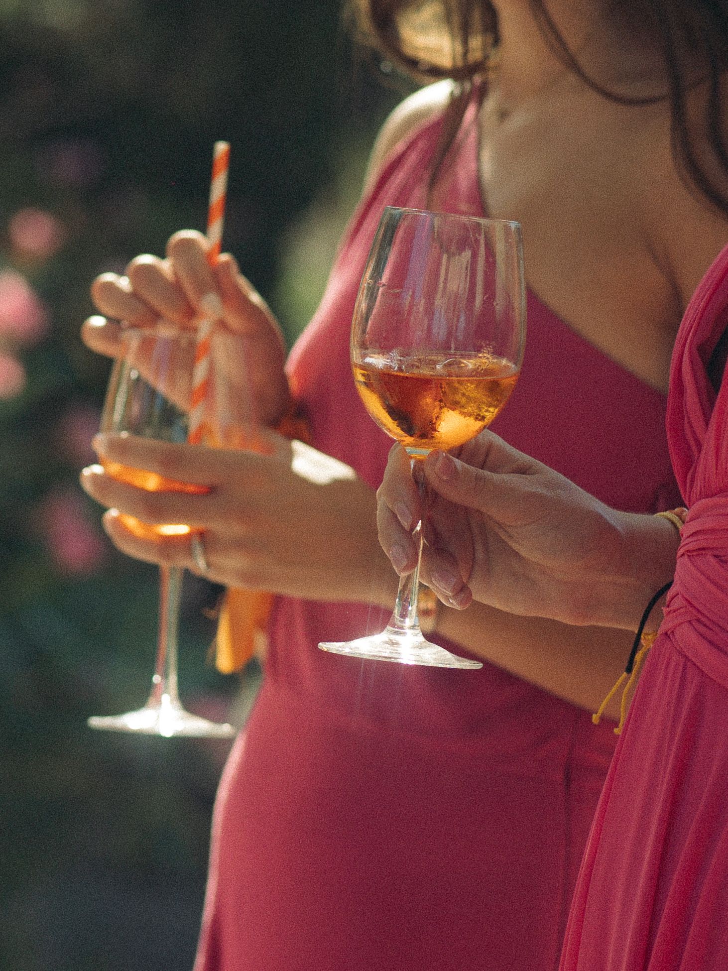 Two women in pink dresses holding glasses of rosé wine outdoors at a garden party.