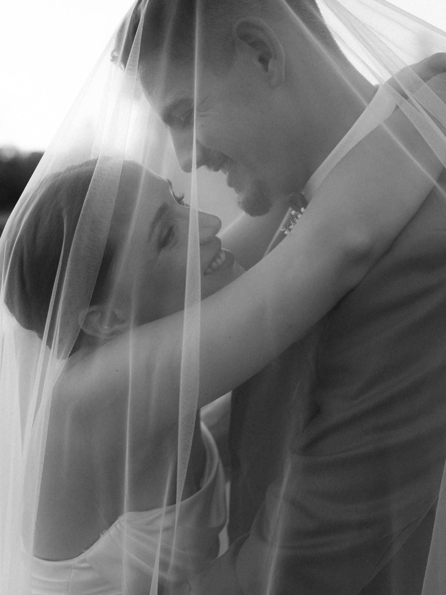 Black and white wedding photo of bride and groom sharing an intimate moment under a flowing veil.