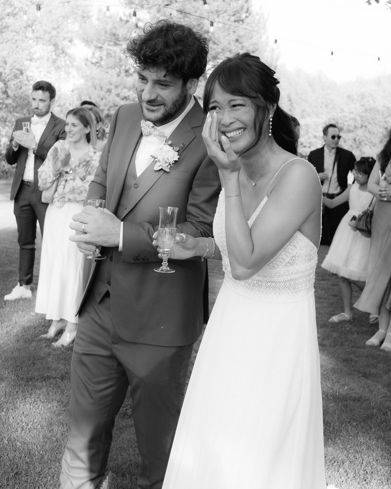 A joyful black and white photo of a couple laughing together at an outdoor wedding celebration.