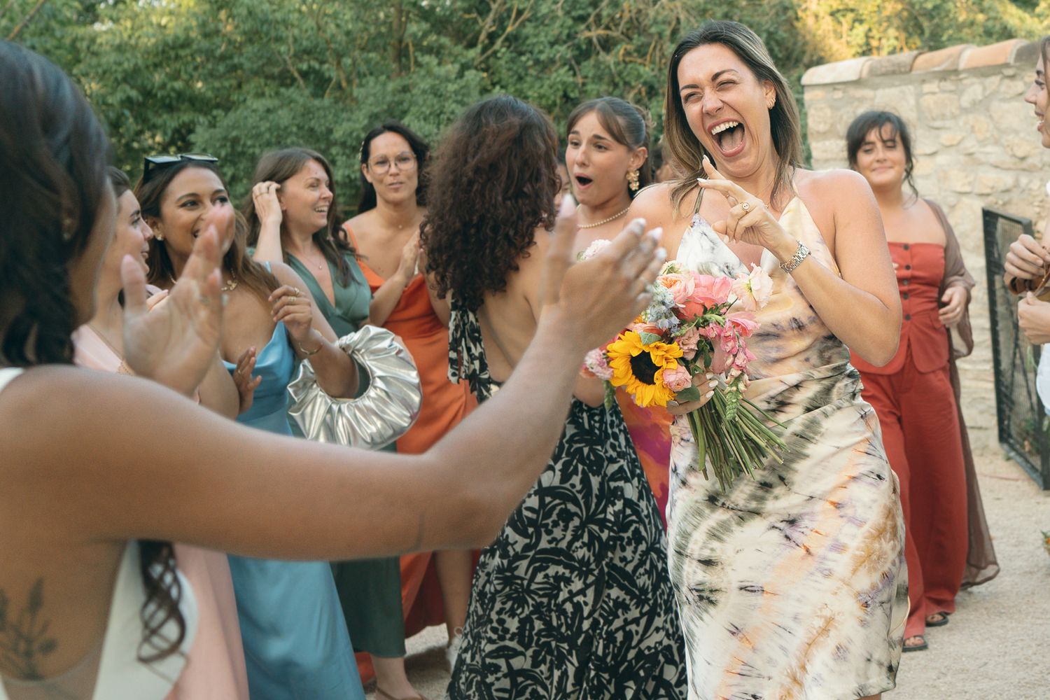 A group of wedding guests enjoying a festive outdoor celebration with dancing and laughter in a sunlit garden setting.