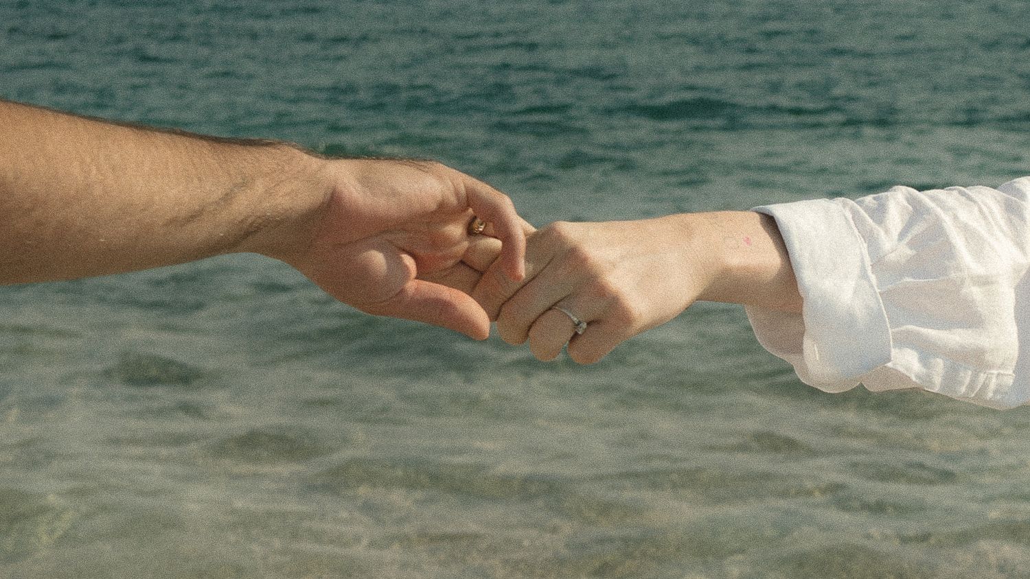 Two hands reaching out to touch each other against a turquoise ocean background in a romantic gesture.