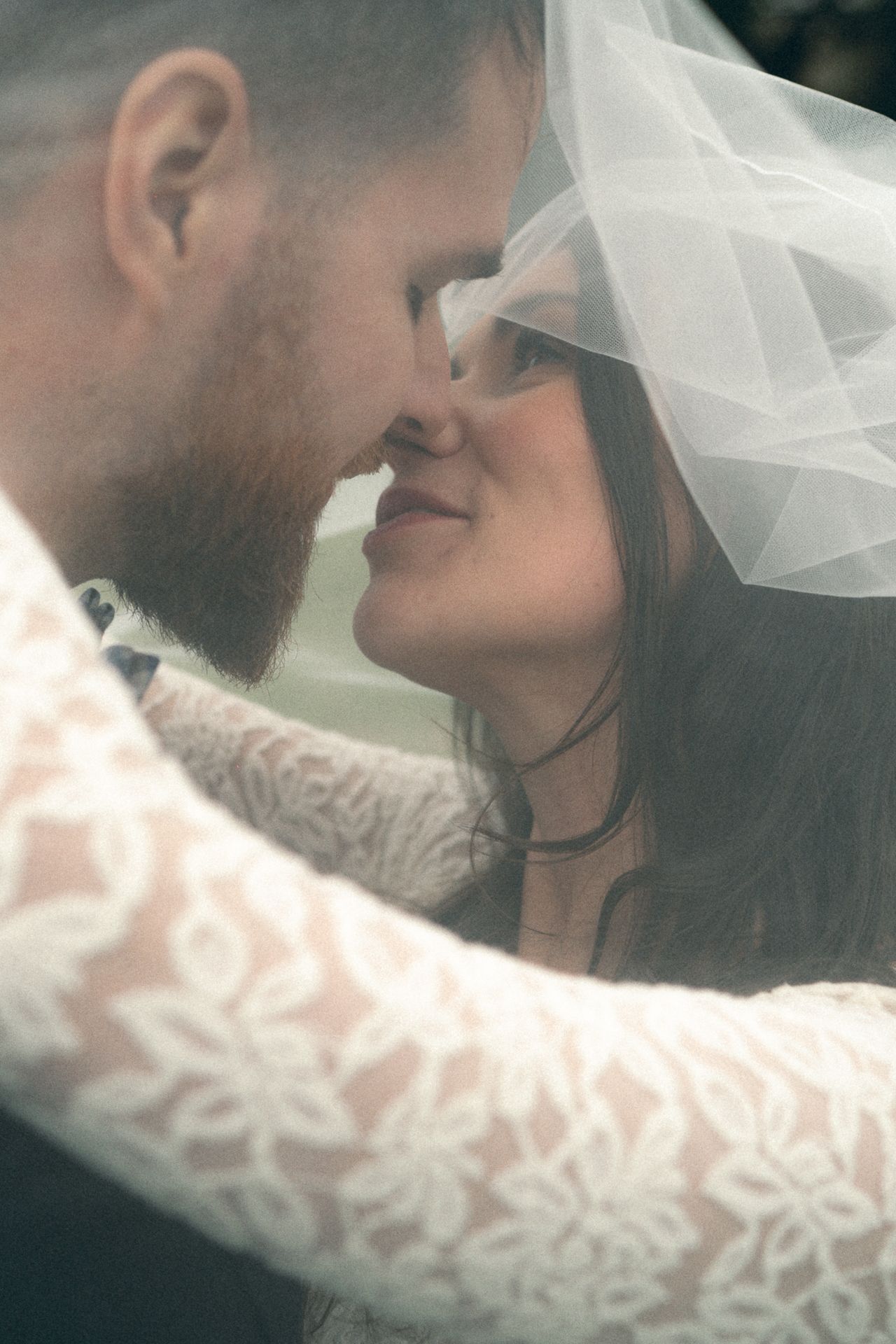 A romantic wedding moment captured in soft focus with delicate lace veil details and an intimate close-up pose.