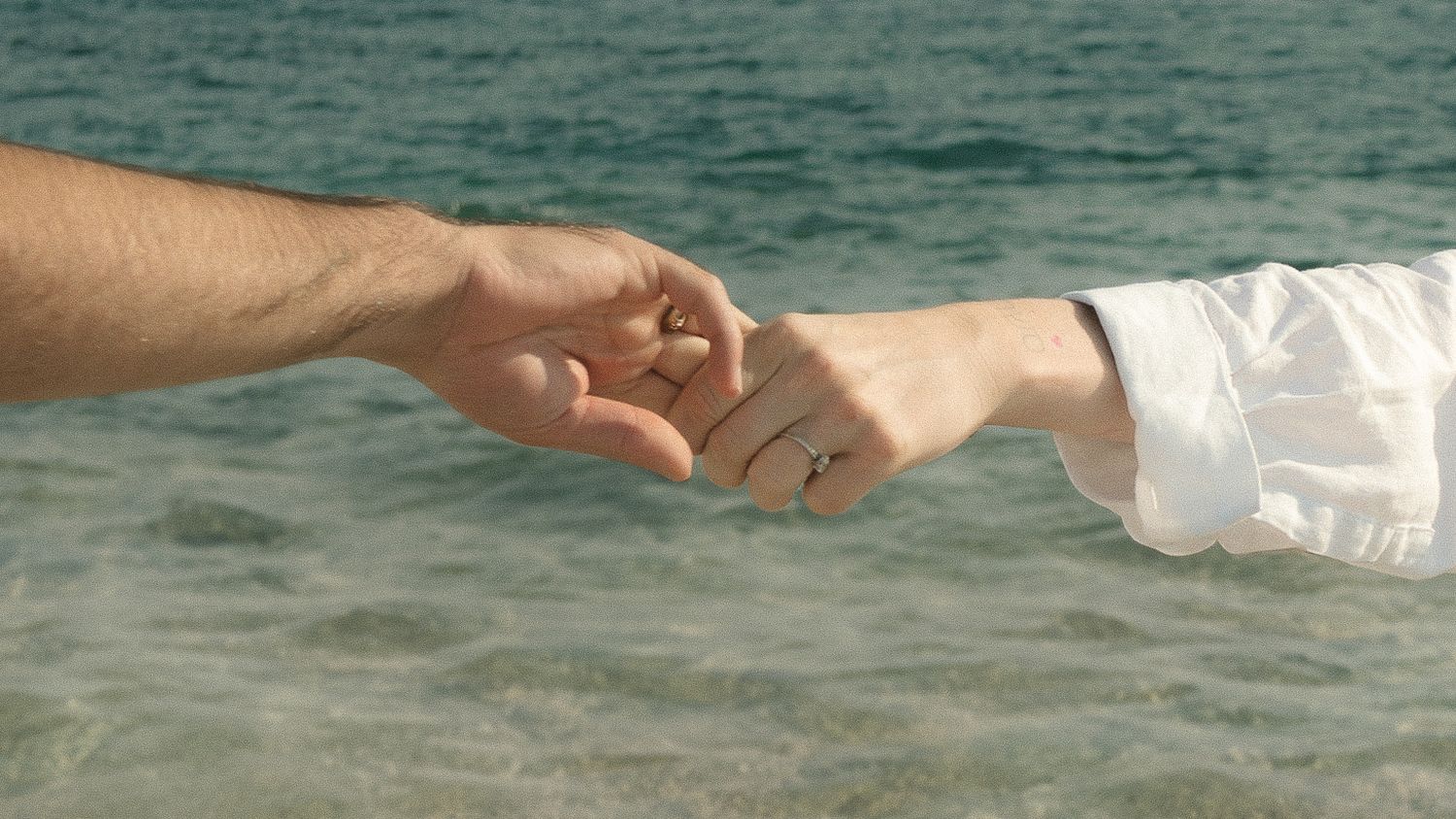 Two hands reaching out to hold each other against a turquoise ocean background.