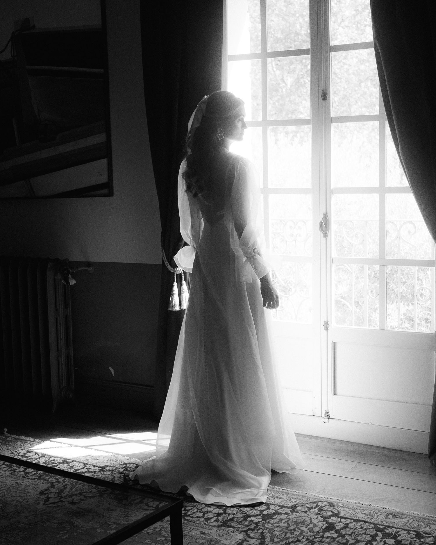 A series of black and white photographs showing a bride in a flowing white dress standing by a bright window.