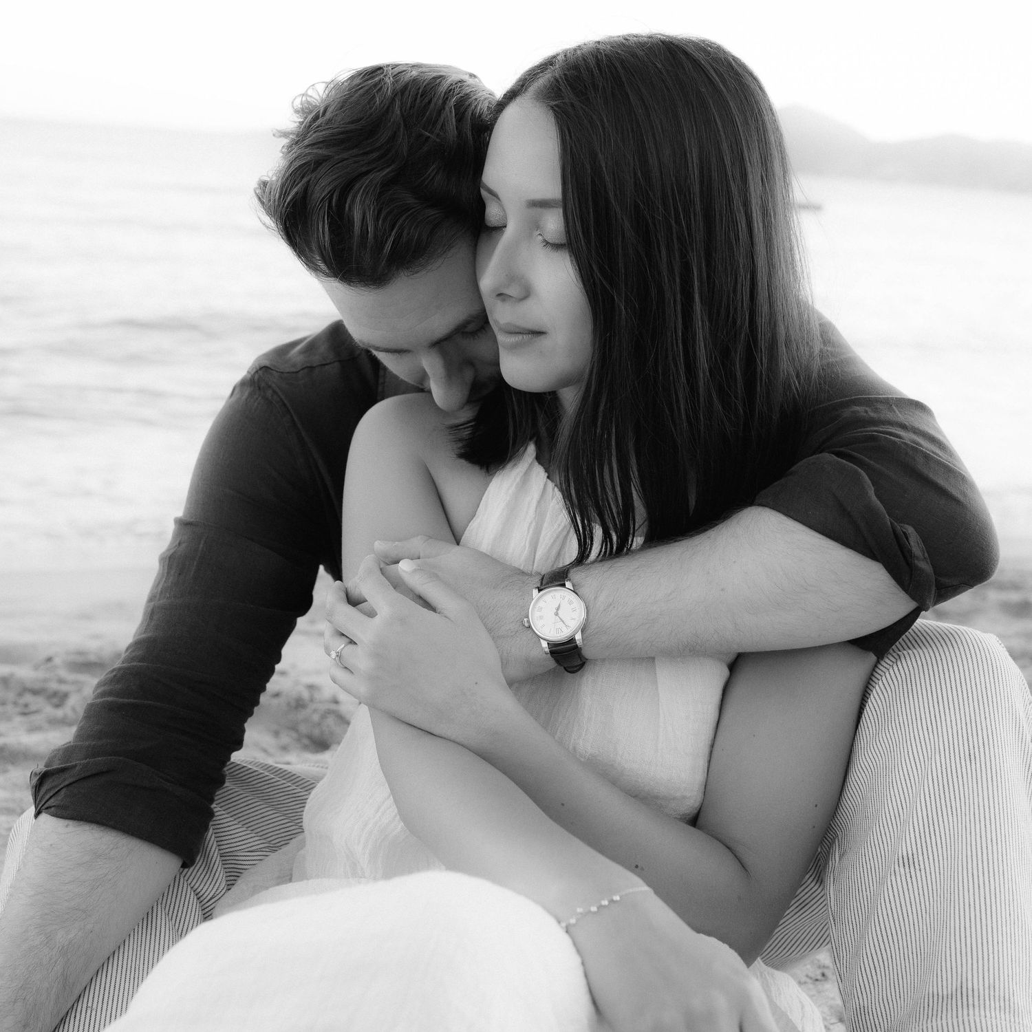 A romantic black and white photo series showing tender moments between a couple embracing on the beach.
