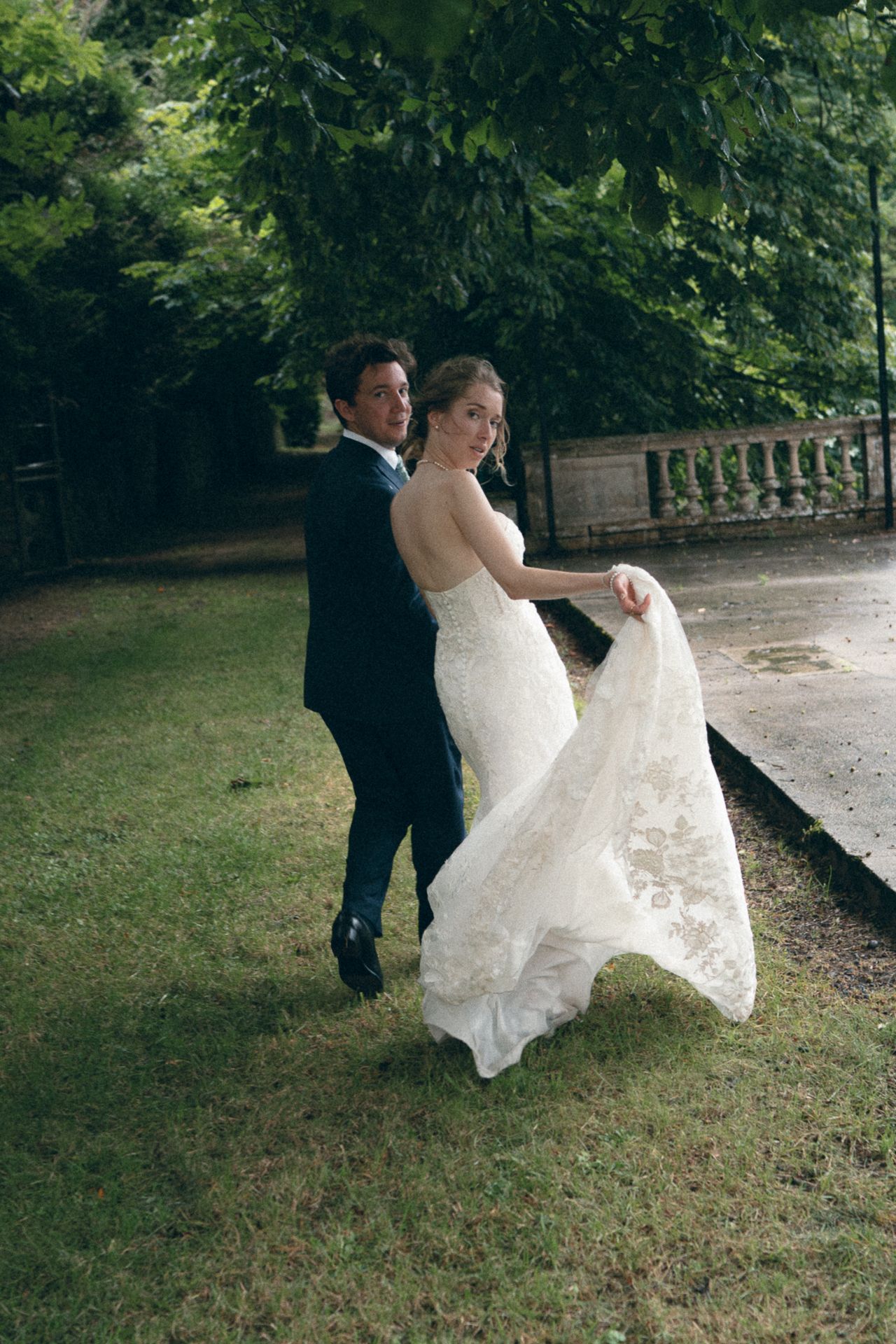 A couple dancing together on grass near a stone wall in an outdoor garden setting.