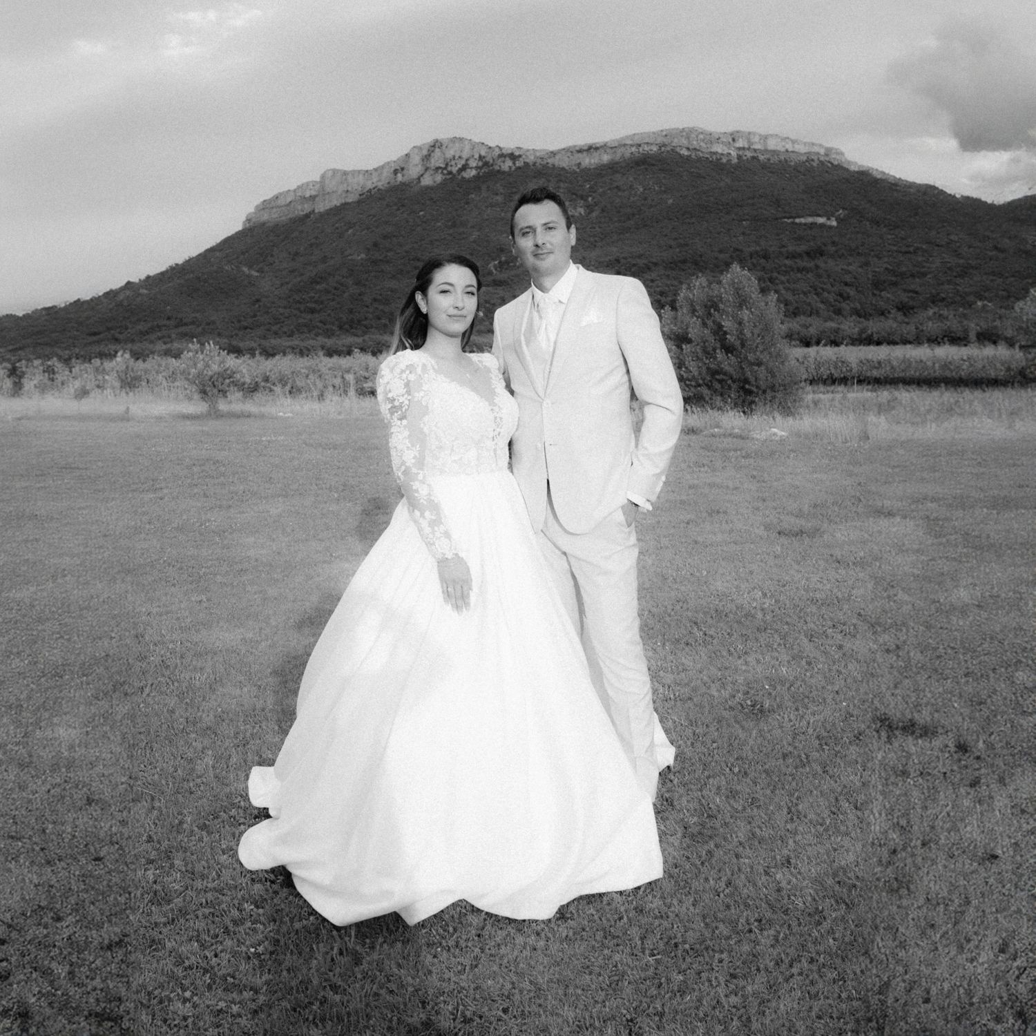 A black and white wedding photo of a couple standing in a field with a mountain backdrop.