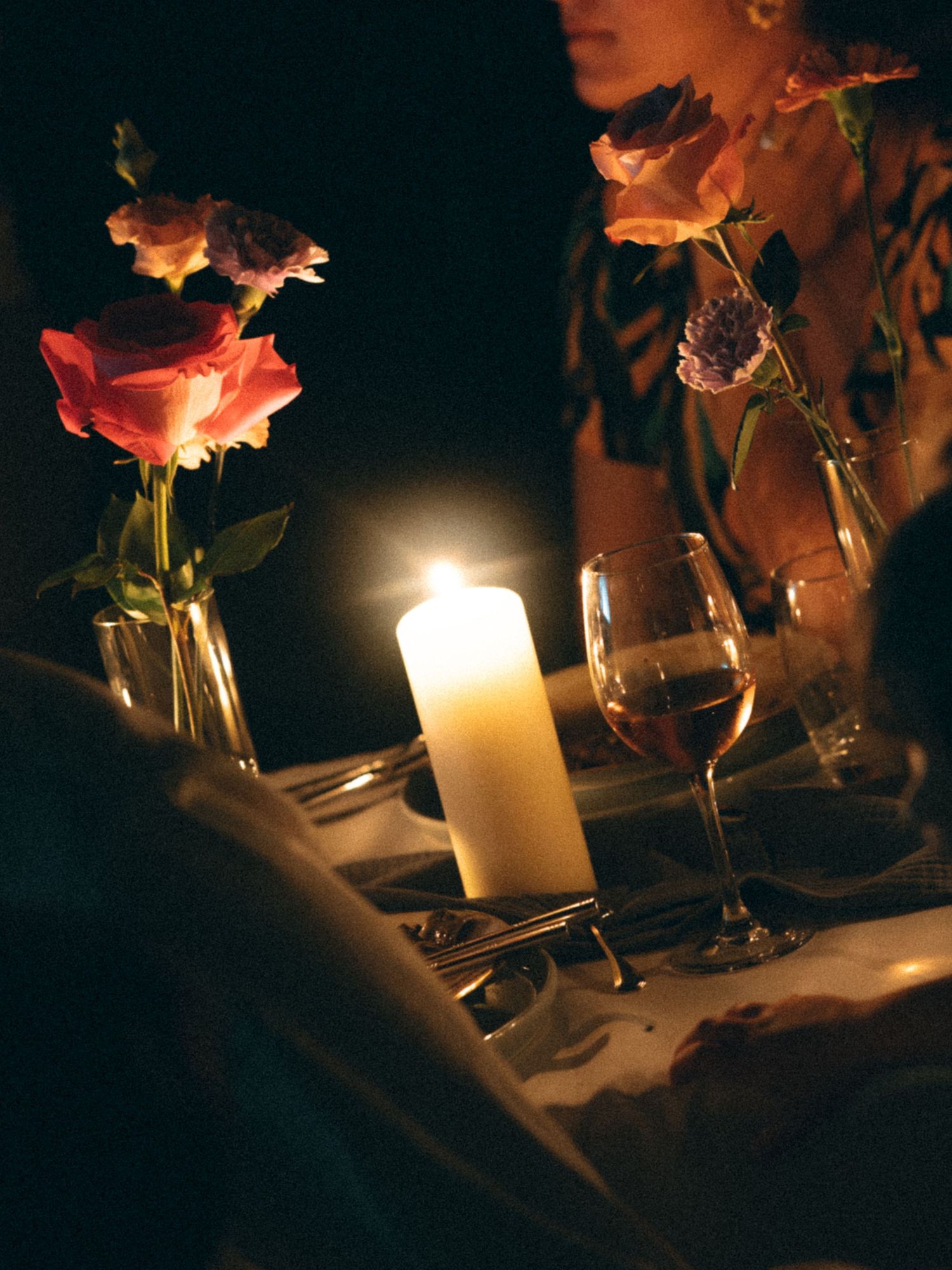 Romantic candlelit dinner table with pink roses in glass vases, a wine glass, and soft glowing candlelight.