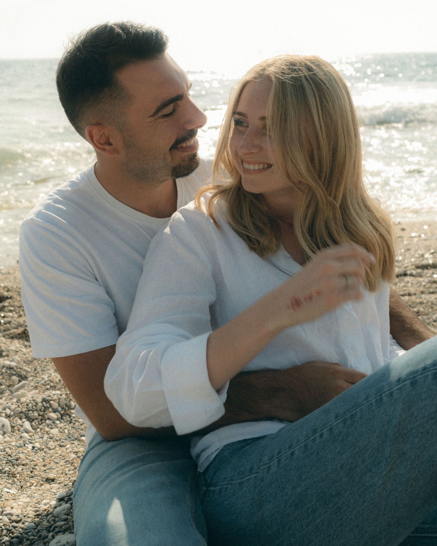 A couple shares a tender moment together while sitting by the ocean on a sunny day.