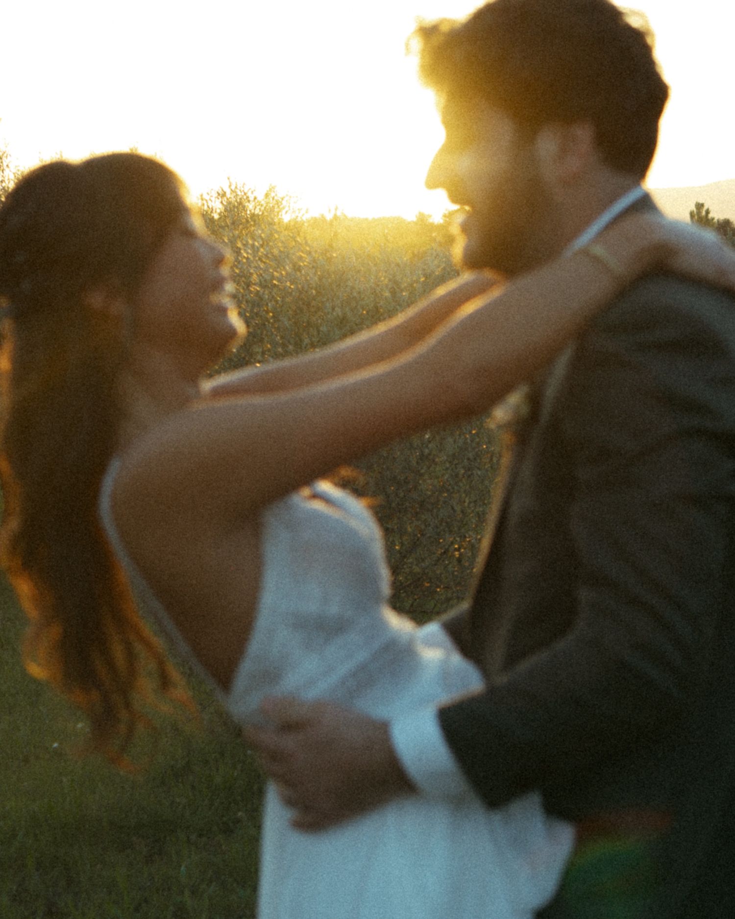 A couple embraces in a romantic dance pose during golden hour sunset in an outdoor setting.