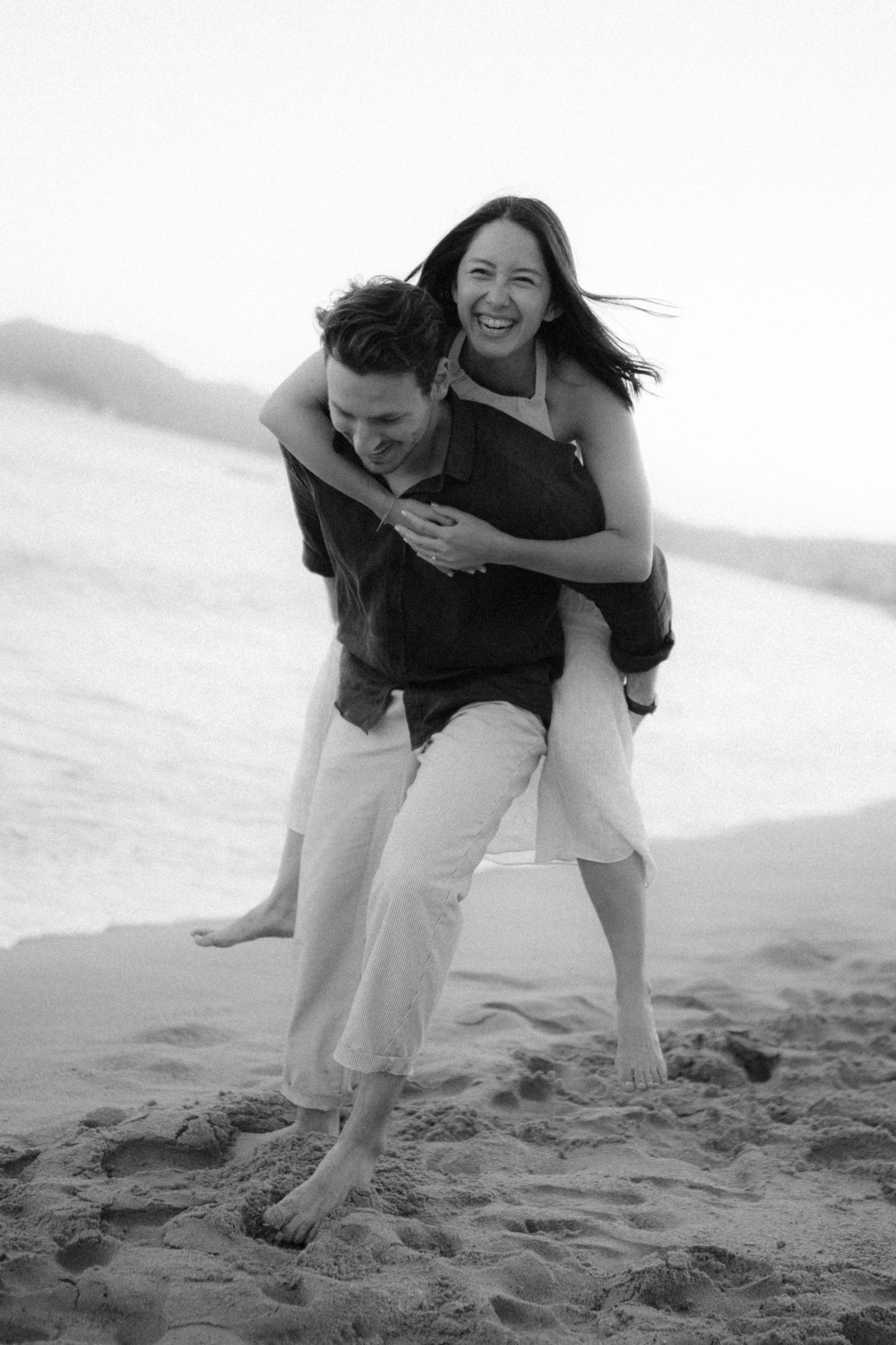 Two people playfully interact on a sandy beach in black and white, creating a joyful sequence of movement.