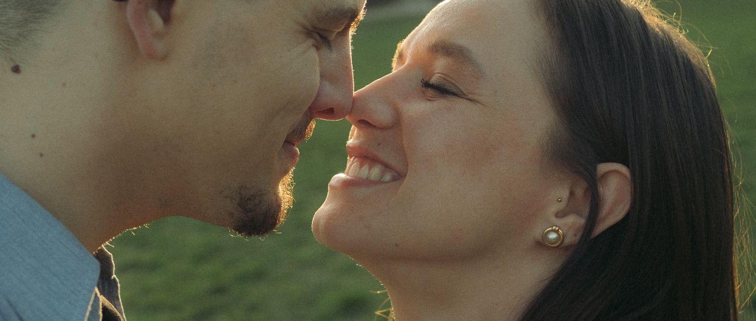 Romantic couple sharing an intimate moment, almost kissing outdoors in golden sunlight with a green background.