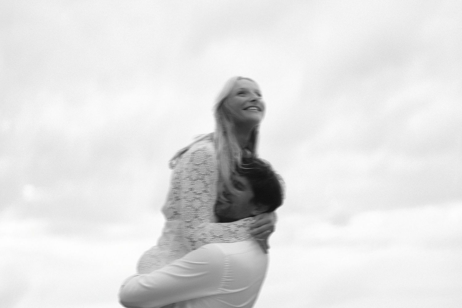 A person wearing a white dress twirls joyfully in an outdoor setting with a cloudy sky backdrop.