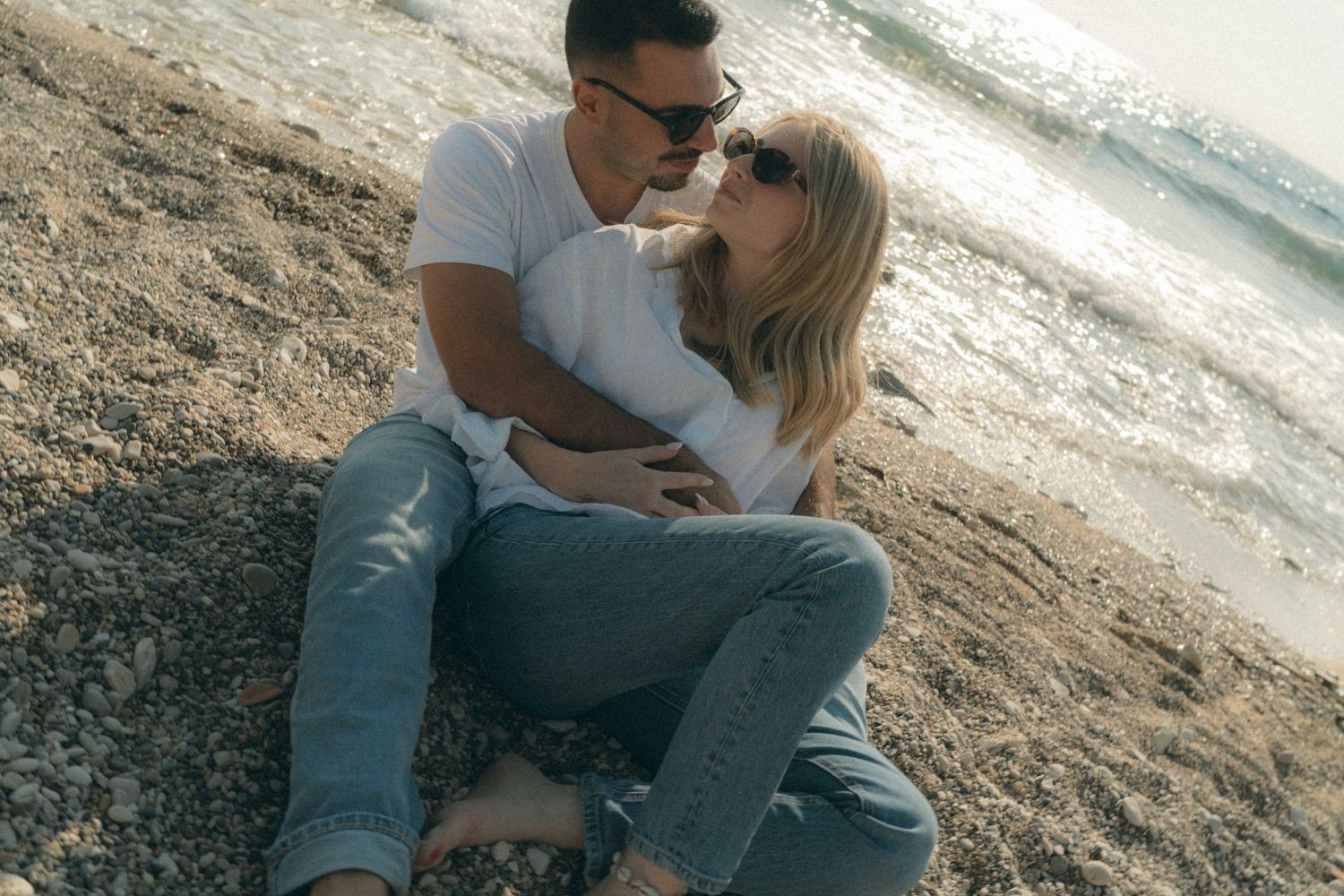 A couple sits together on a rocky beach sharing intimate moments at sunset.
