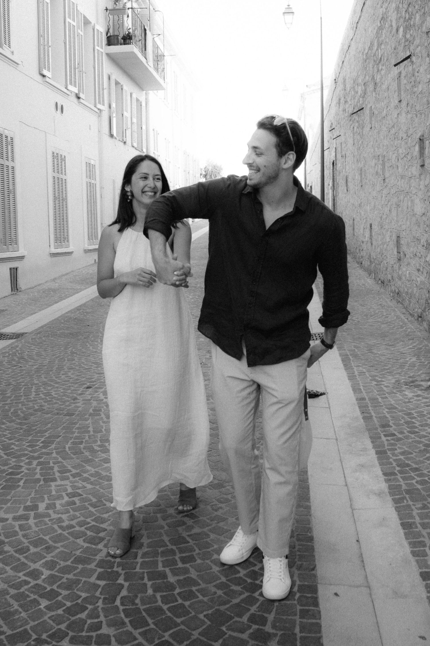 A couple walks together down a narrow cobblestone street wearing contrasting black and white outfits.