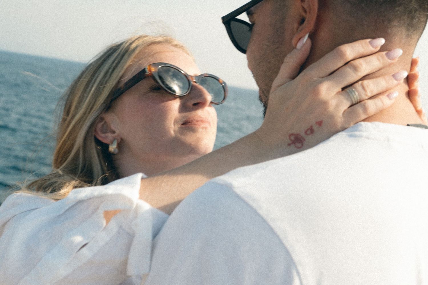 A romantic couple in sunglasses embraces on a boat with the ocean visible in the background.