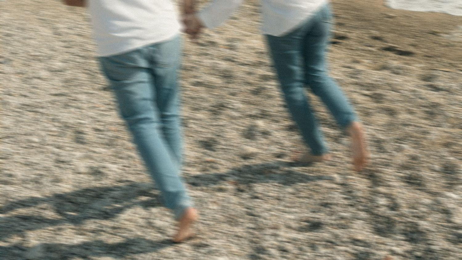 A sequence of feet walking along a sandy beach shore with waves lapping at their feet.