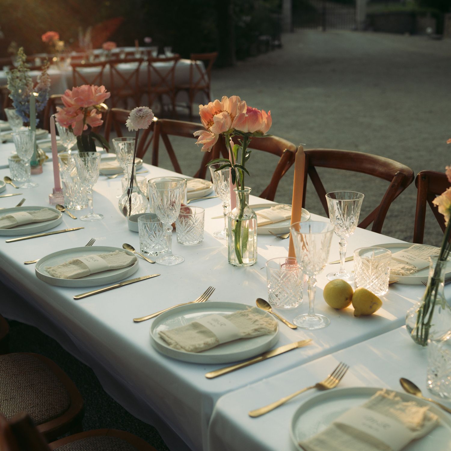 An elegant table setting with white linens, glassware, and soft peach floral centerpieces for a formal dining event.