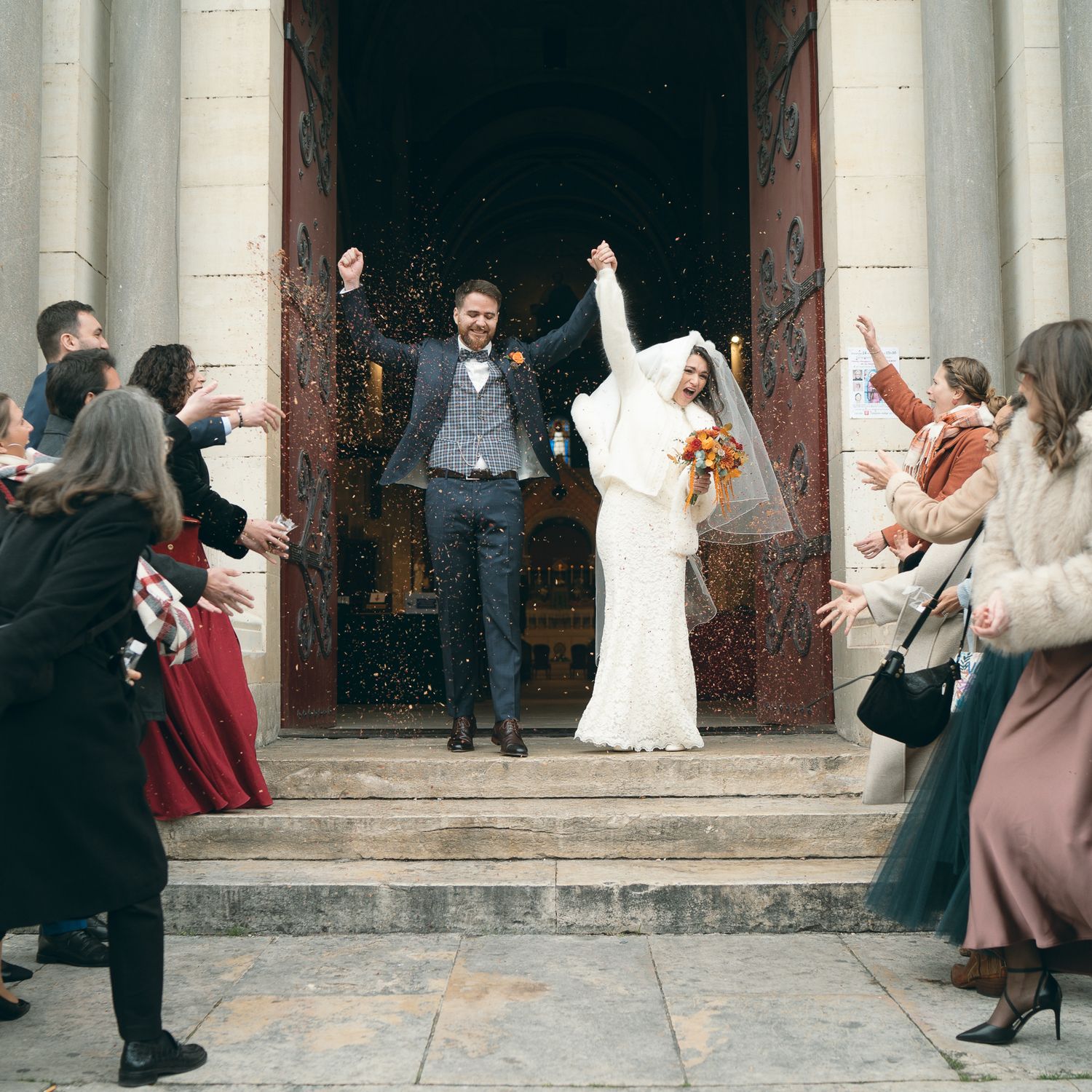 Wedding guests throw rice and confetti at the church entrance as newlyweds exit after their ceremony.