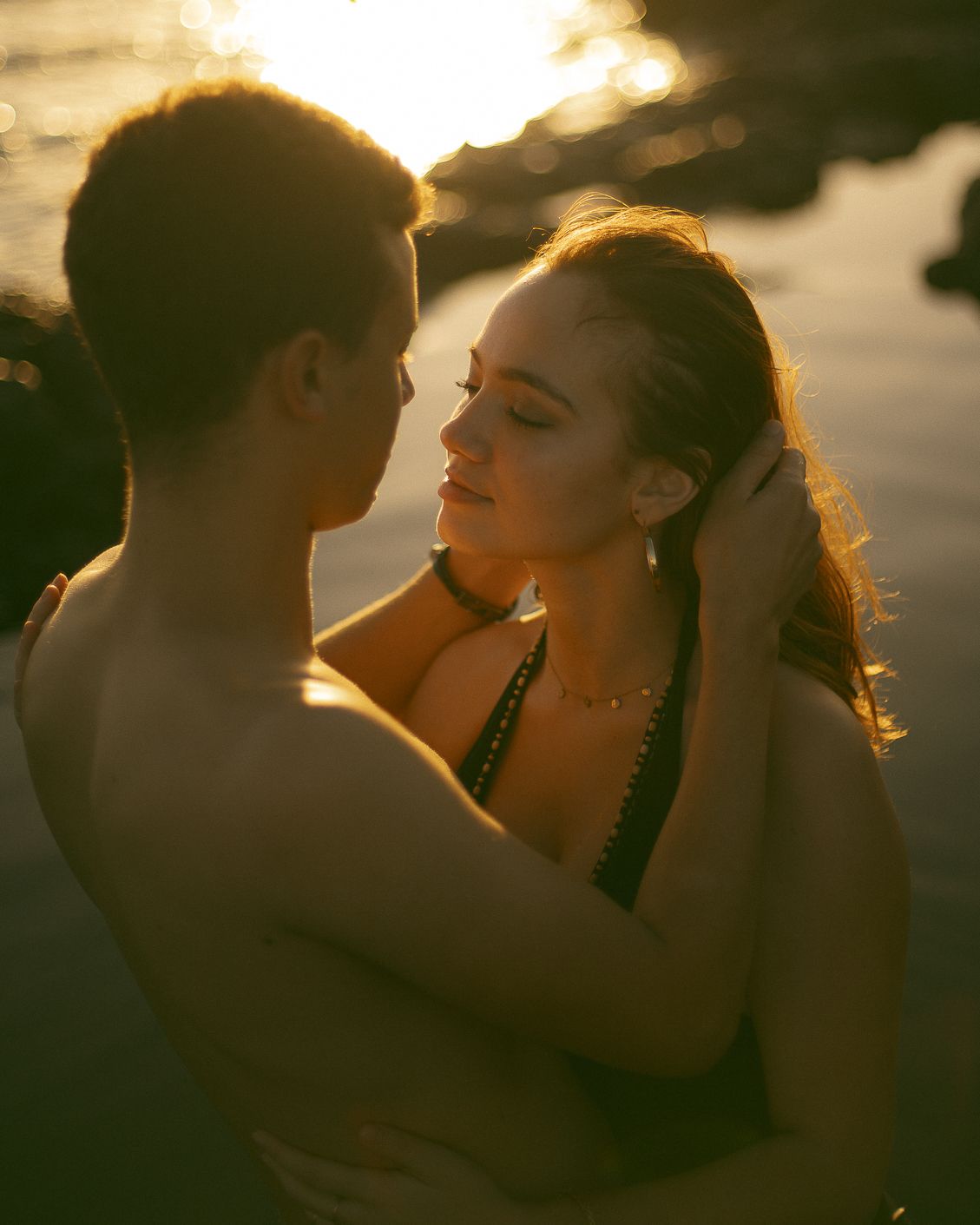 Silhouetted couple embracing in romantic sunset light with golden backlit glow.